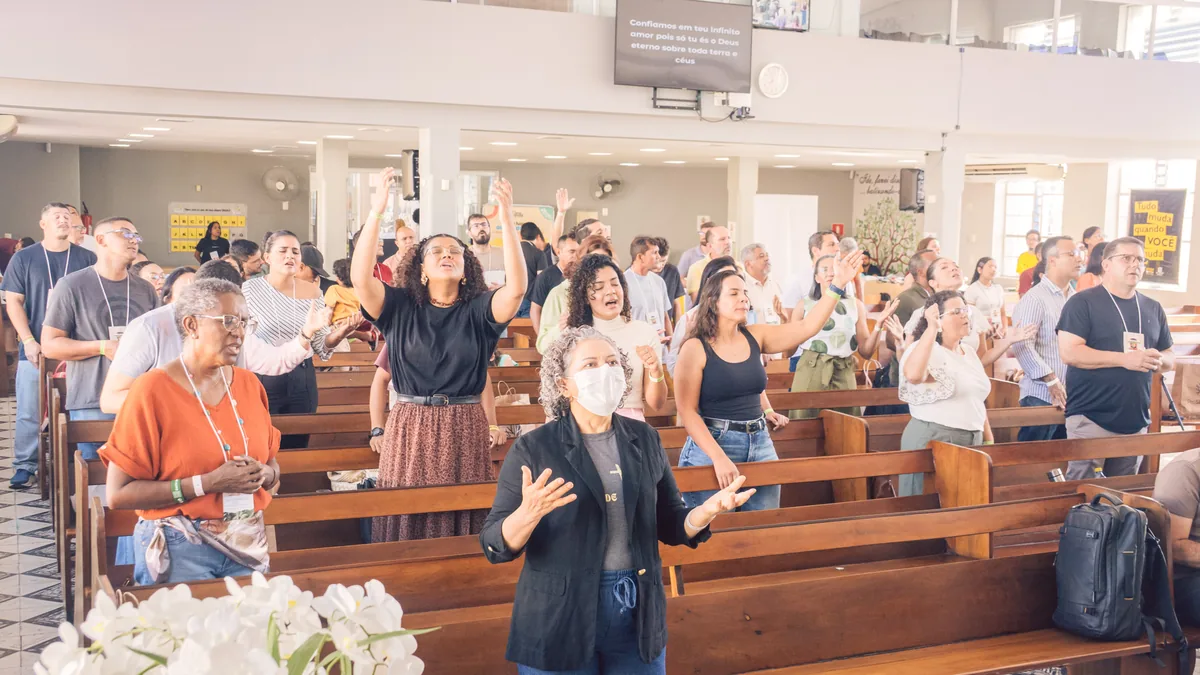 Kongressteilnehmende stehen in den Kirchenbänken und loben Gott mit erhobenen Händen