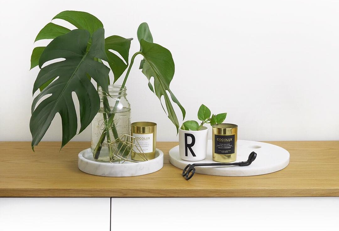 gold and marble home decor items with monstera and ivy leaves against white backdrop