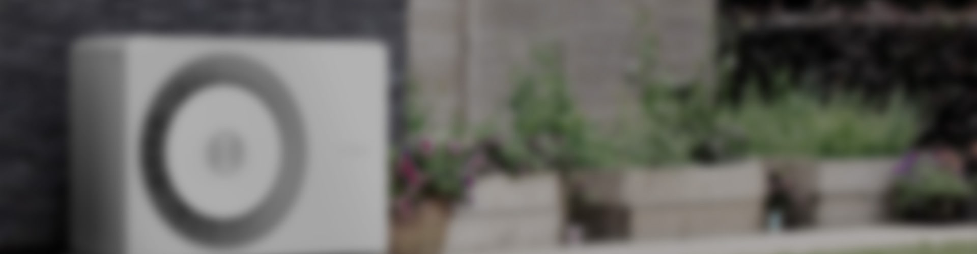 Wärmepumpe in einem Garten in verschwommener Optik als Hintergrundbild