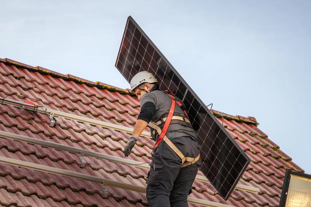 Ein Enpal Monteur, der ein Solarmodul auf ein Dach trägt, um es dort auf den Montageschienen zu befestigen.