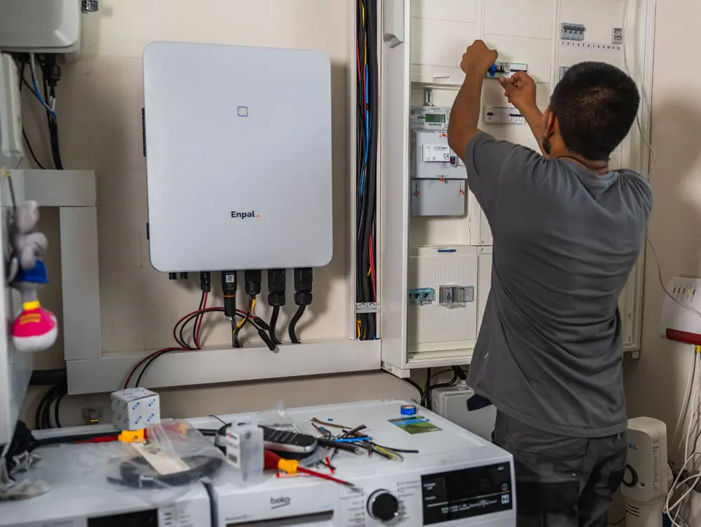 Ein Enpal Handwerker bereitet die Elektrik in einem Hauswirtschaftsraum auf die PV-Anlage vor. Man sieht auch einen Enpal Wechselrichter an der Wand hängen.