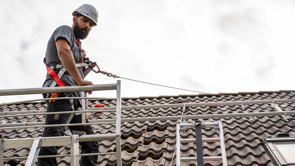 Ein Enpal Monteur steht auf einem Hausdach, bevor die Installation einer PV-Anlage beginnt. Auf dem Dach sieht man auch Montageschienen, einen Fallschutz und eine Leiter.