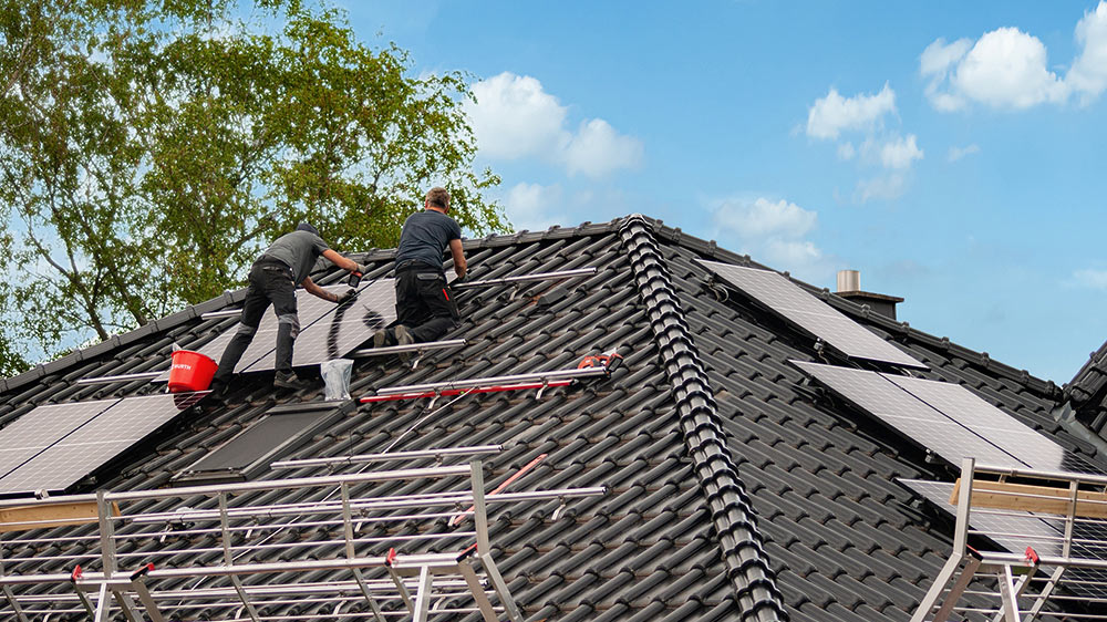 Zwei Enpal Monteure bei der Montage einer Enpal Solaranlage. Man sieht PV-Module, Montageschienen und den Fallschutz für die Handwerker
