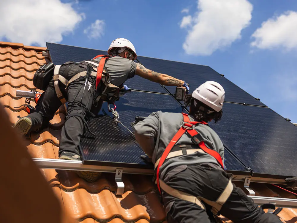 Zwei Enpal Handwerker bei der Montage einer Solaranlage auf einem Hausdach mit hellbraunen Ziegeln