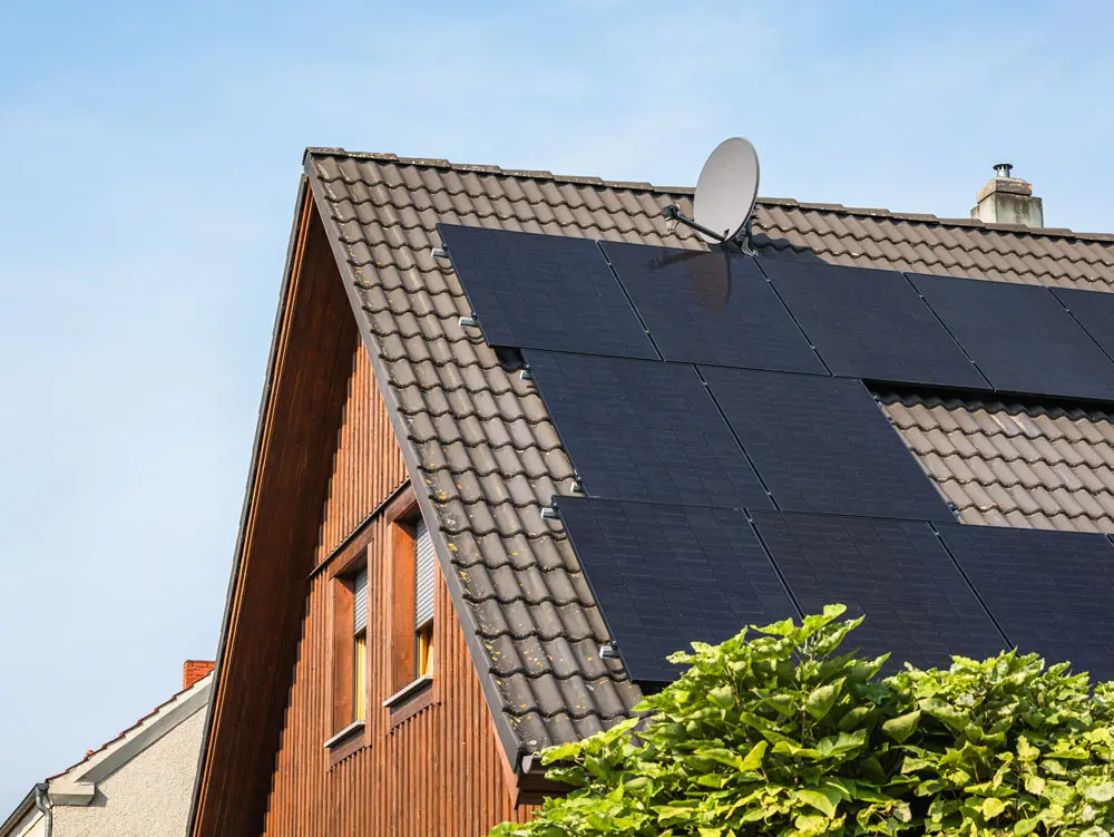 Ein Haus mit Holzverkleidung und einem braunen Dach. Auf dem Dach ist eine Photovoltaikanlage installiert.