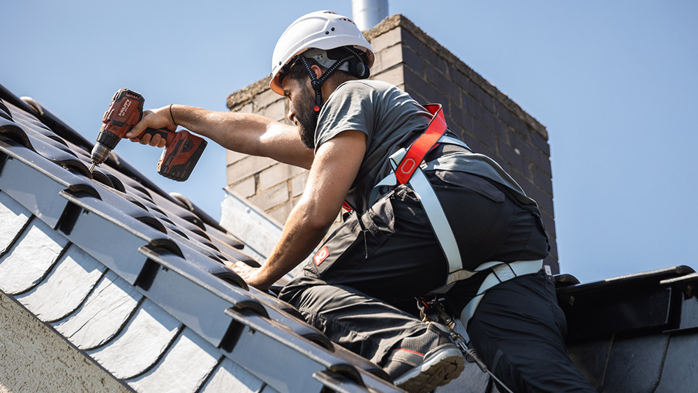 Ein Enpal Monteur auf einem Hausdach bei der Vorbereitung der Dachziegel für die Montage einer Solaranlage.