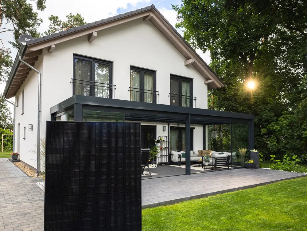 Ein Full-Black Solarmodul steht auf einer Terrrasse vor dem Wintergarten eines weißen Hauses.