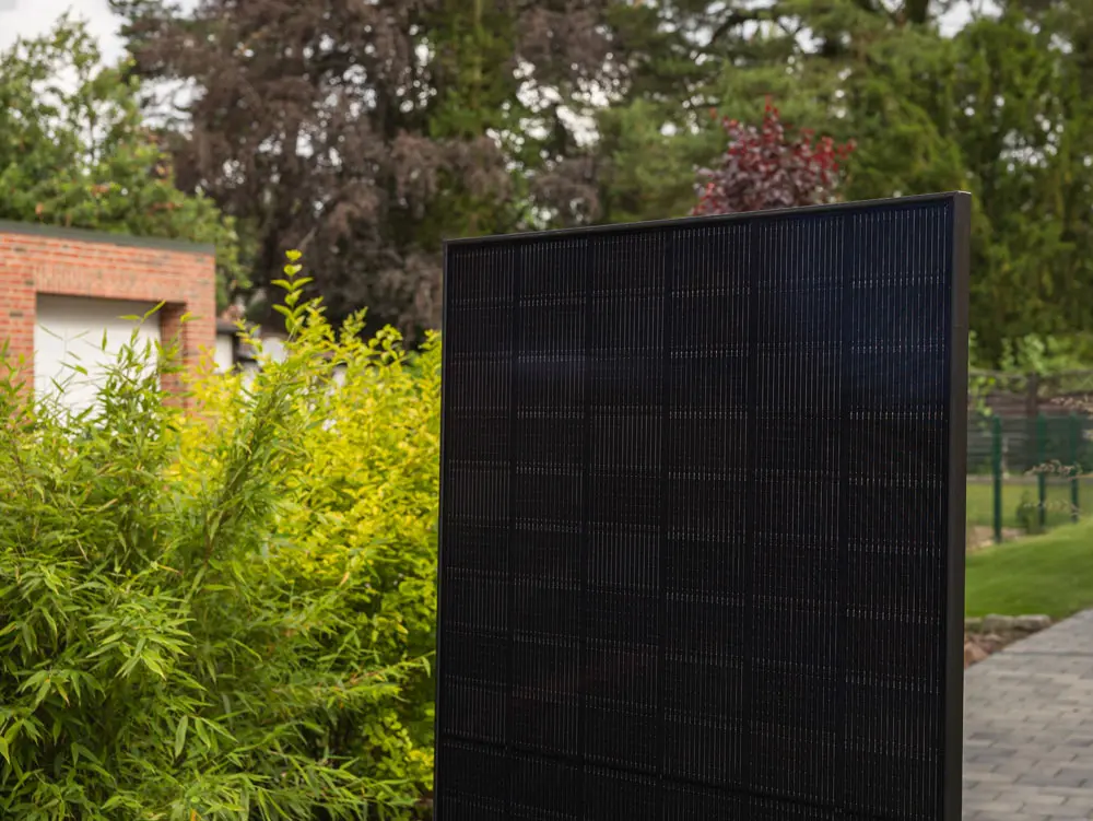 Ein Full-Black Solarmodul, das in einer Einfahrt neben einer Hecke steht.