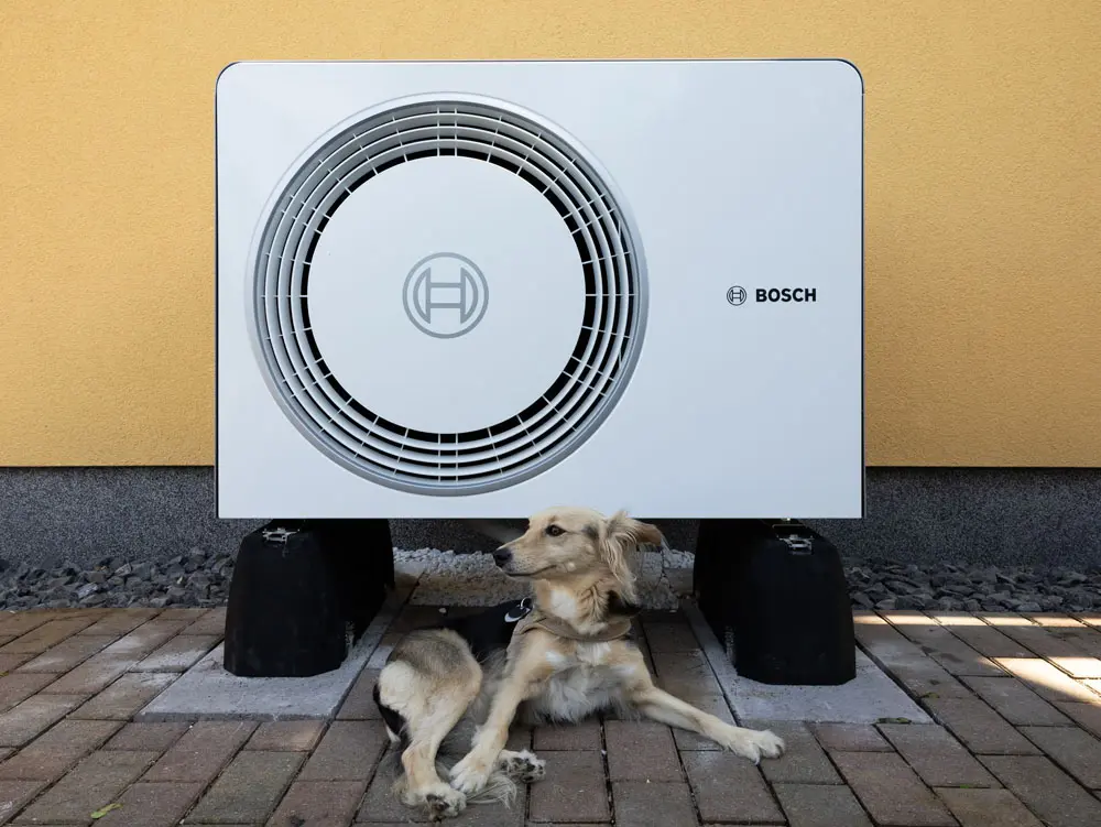 Installierte Bosch Wärmepumpe vor gelber Hauswand mit Hund davor
