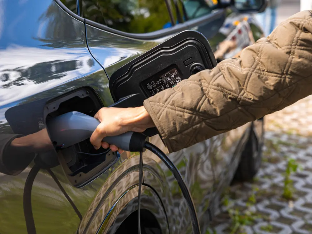 Eine Hand steckt den Stecker einer Wallbox in ein E-Auto