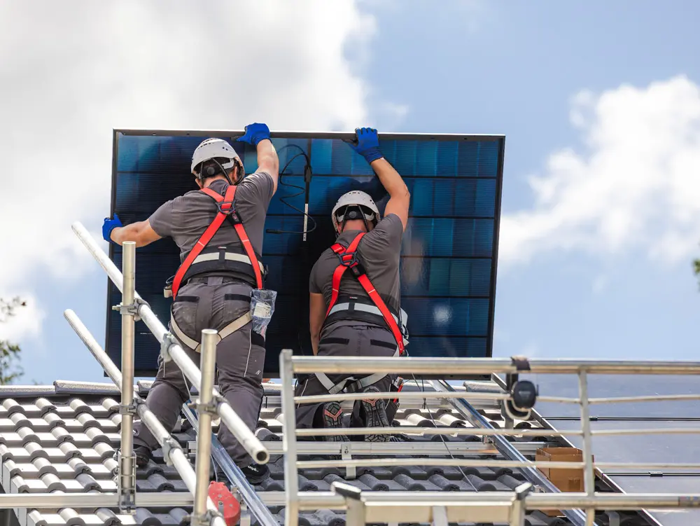 Zwei Enpal-Monteure mit einem Solarmodul auf einem Dach mit Gerüst.