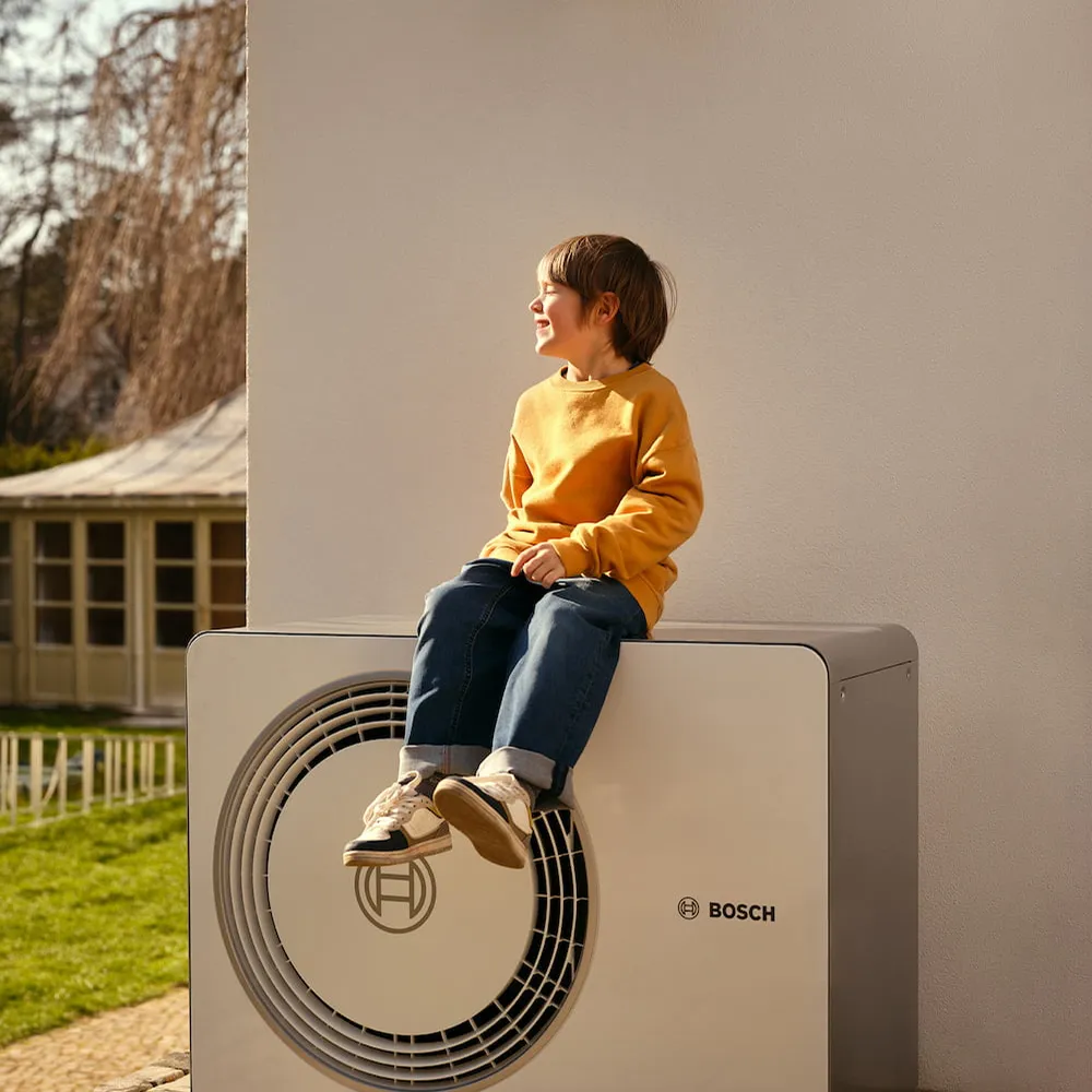 Junge sitzt auf Enpal Wärmepumpe vor einer Hauswand