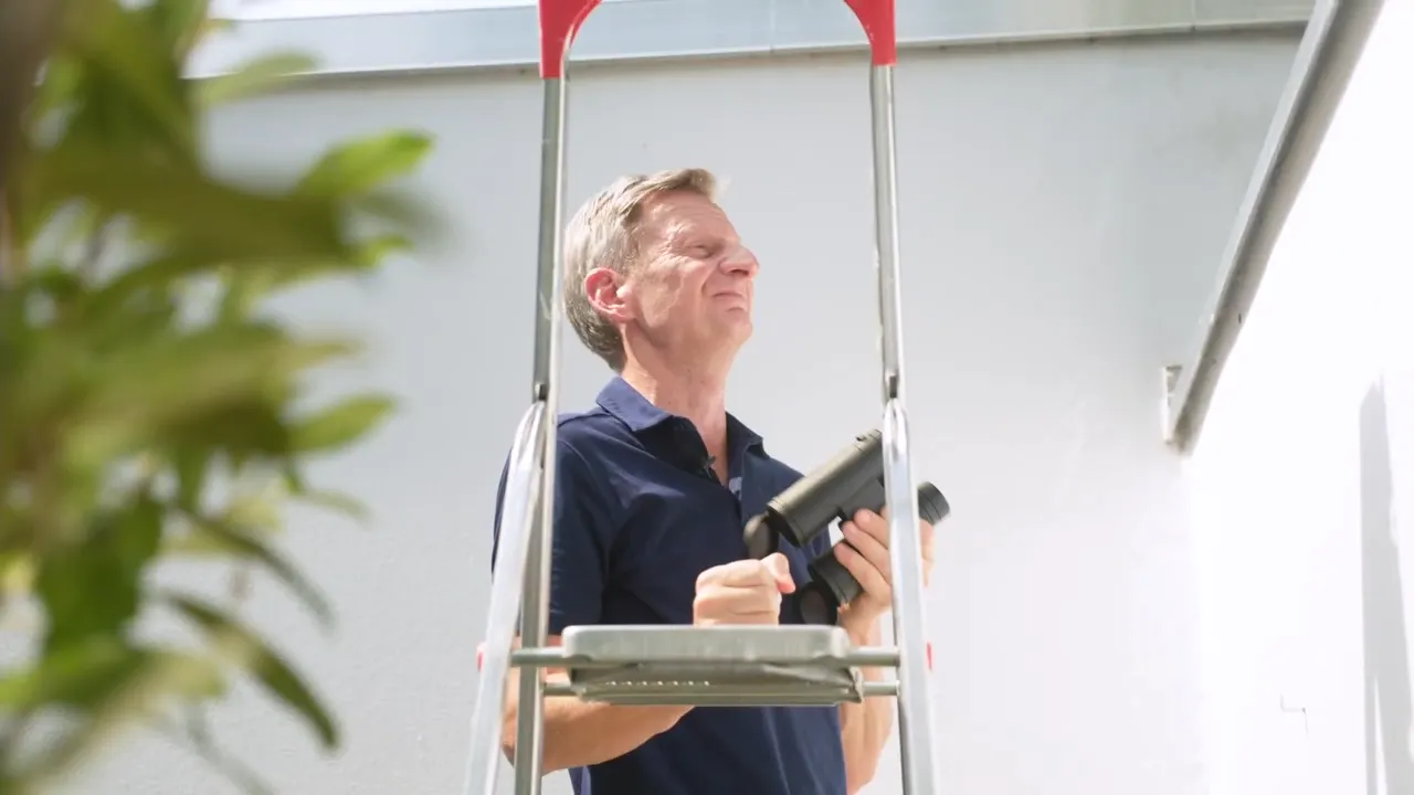 Michael Kesser steht auf einer Leiter und schaut sich das Dach eines Hauses an