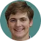 Smiling young man with short brown hair against a teal circular background.