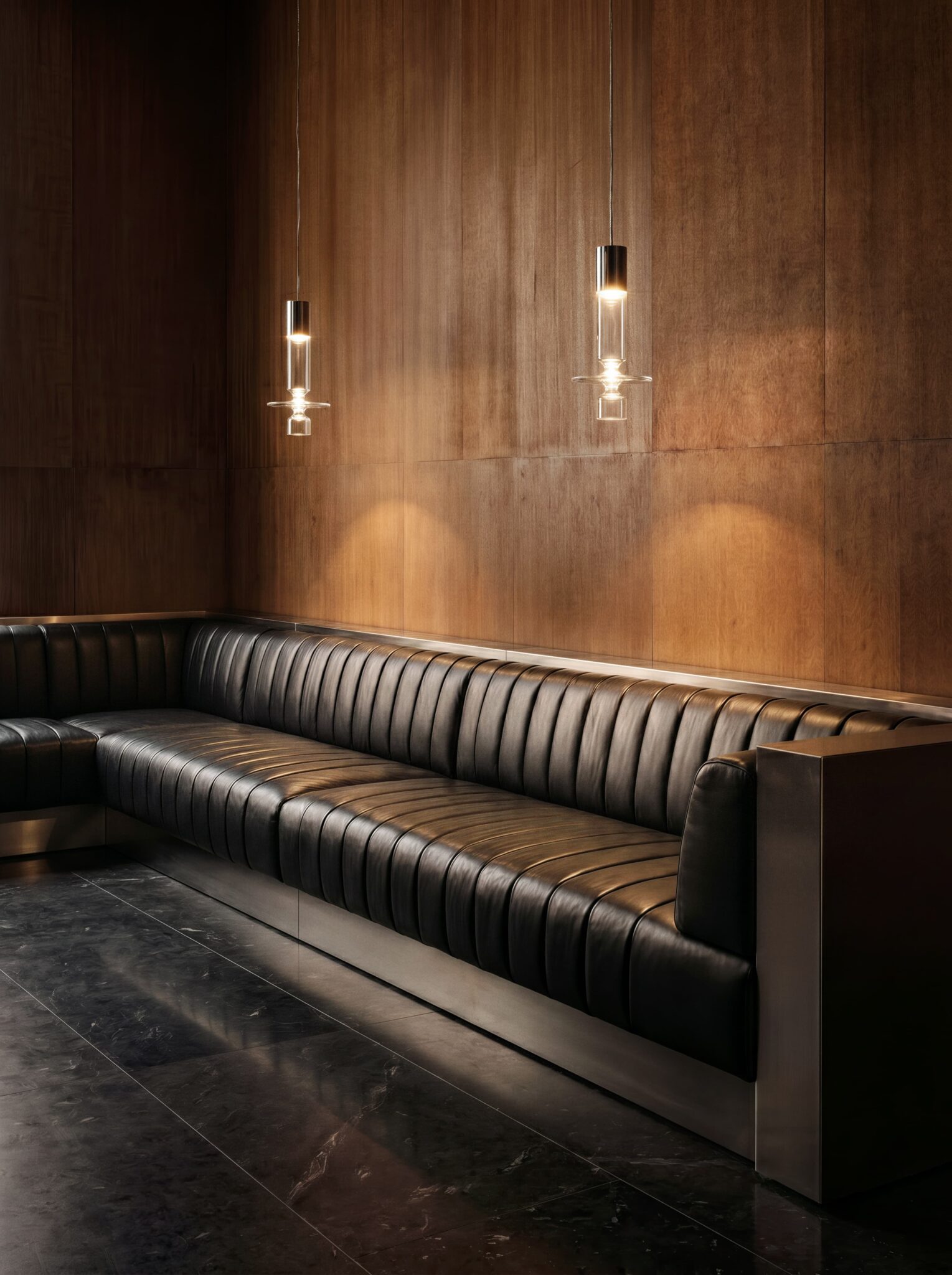 Two Filamento Vertical glass pendants above black leather seating against a warm timber wall.