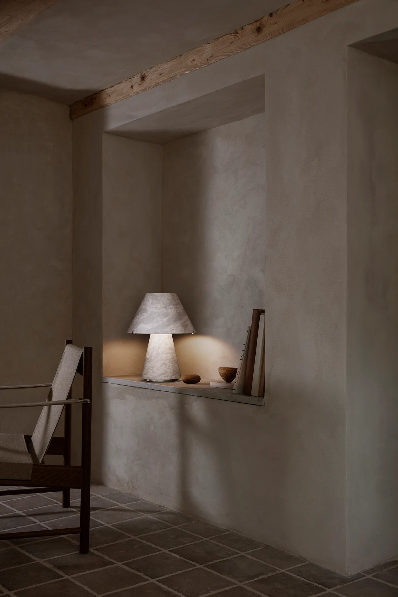 A pale marbled Upglas table lamp illuminating a console beside a chair in a warm, textured interior.