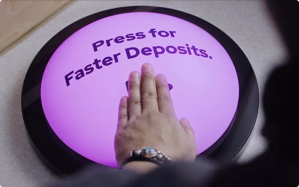 Hand pressing a large round purple button labeled 'Press for Faster Deposits.'
