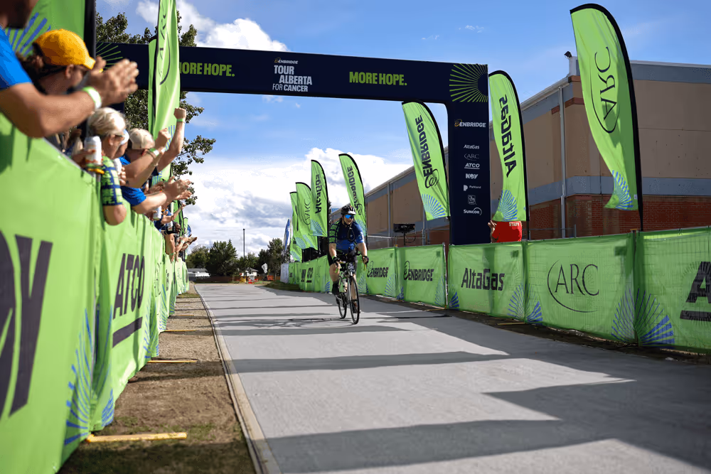 Cyclist riding towards the finish line at the Enbridge Tour Alberta for Cancer event with spectators cheering on the side.