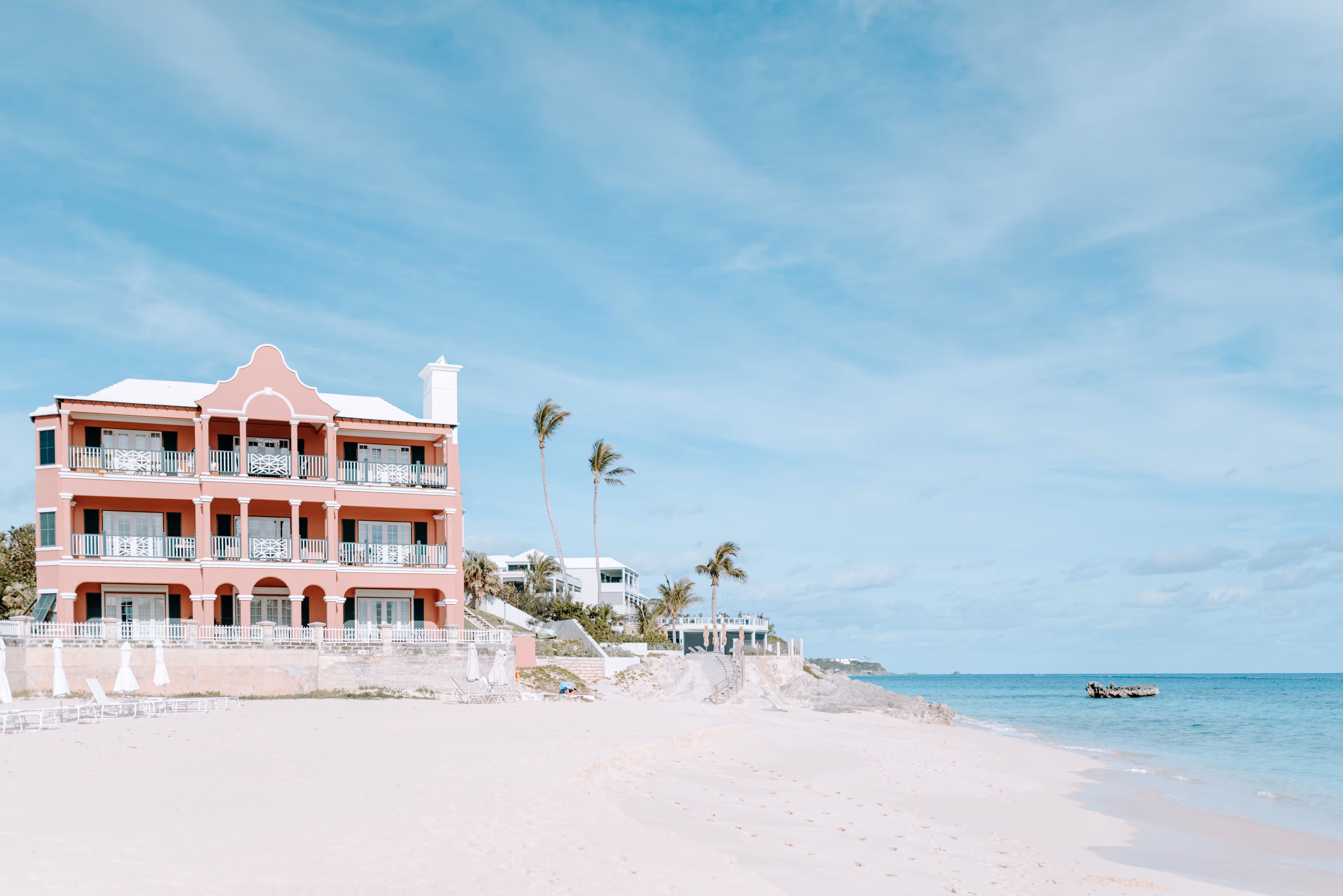 Pink multi floored building next to palm trees on white sand beach