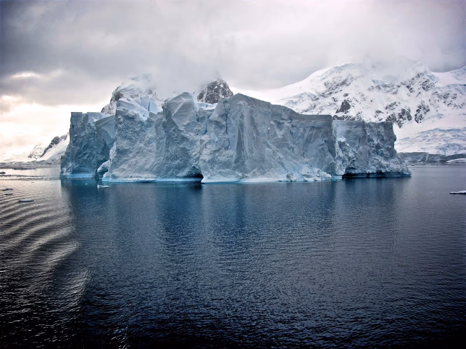 Glacier surrounded by water and icy mountains, with dark gray clouds in the sky
