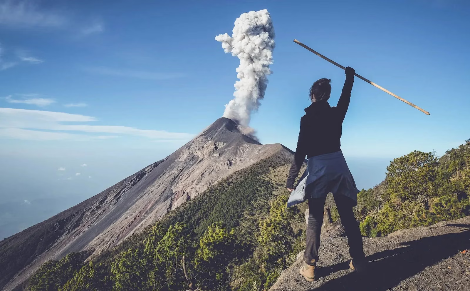 Woman hiking to volcano with smoke and trees in background