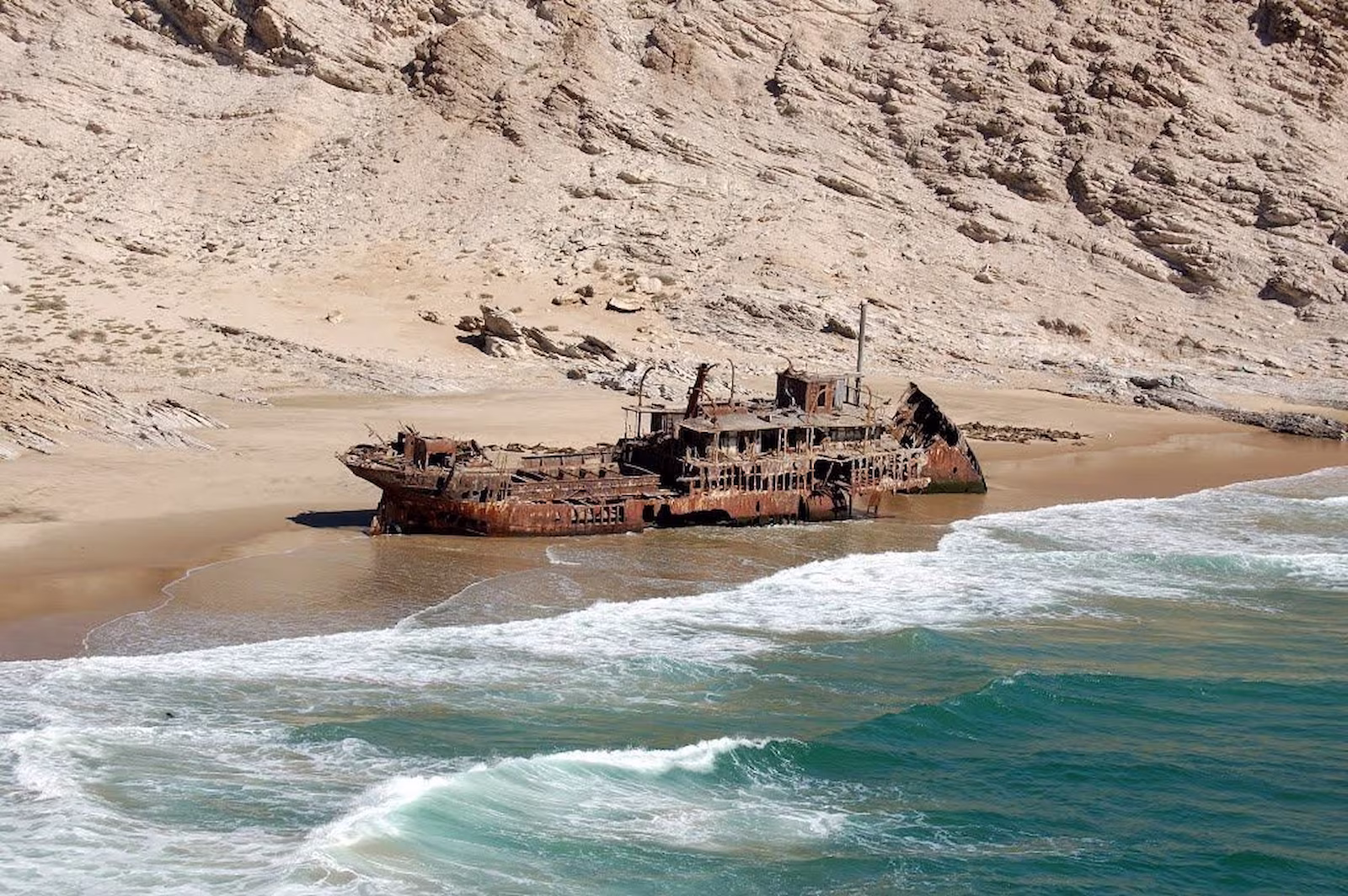 Shipwrecked boat in desert with ocean and sand mountains