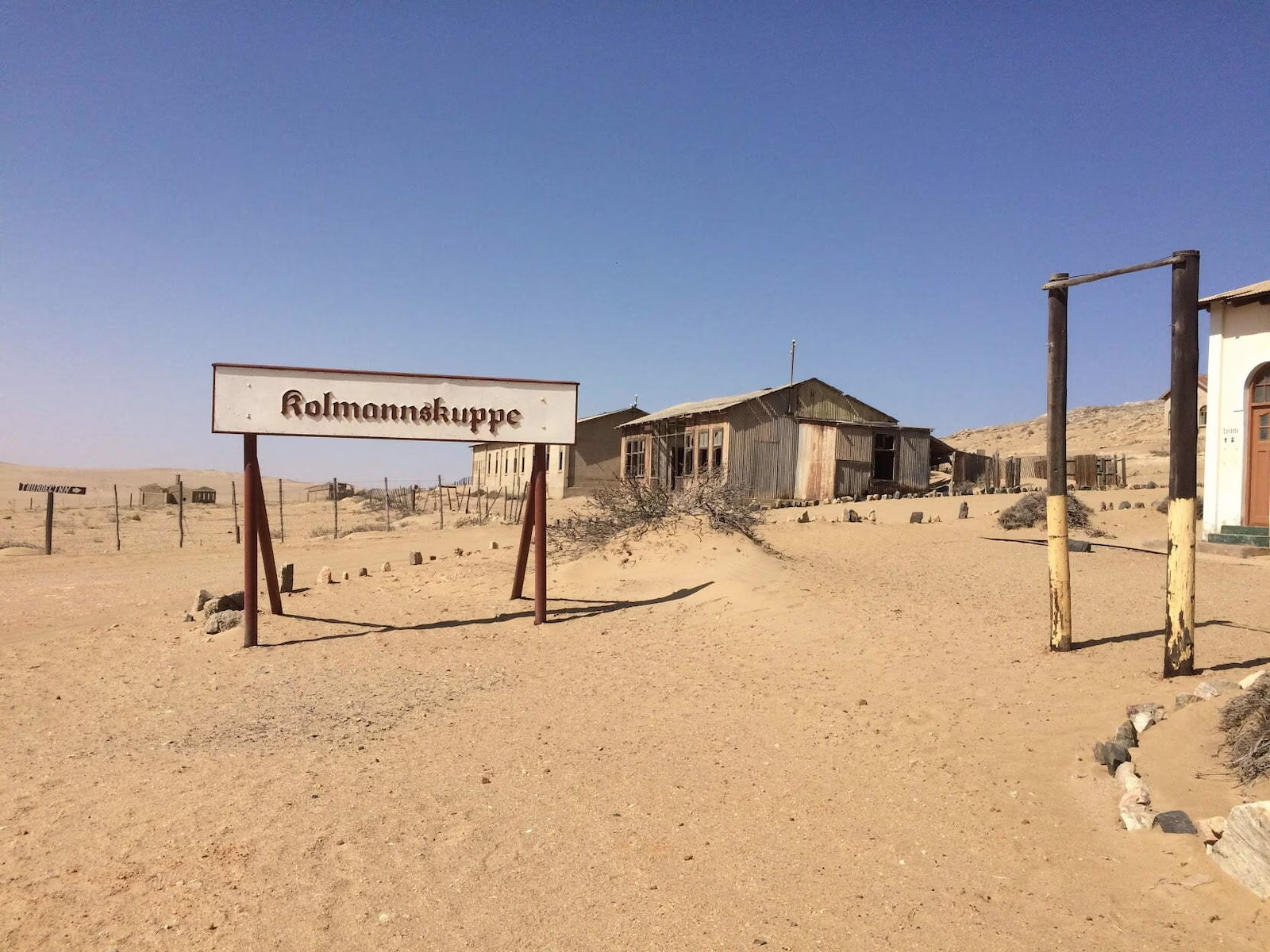 Sign for Kolmanskop with abandoned buildings in background in desert
