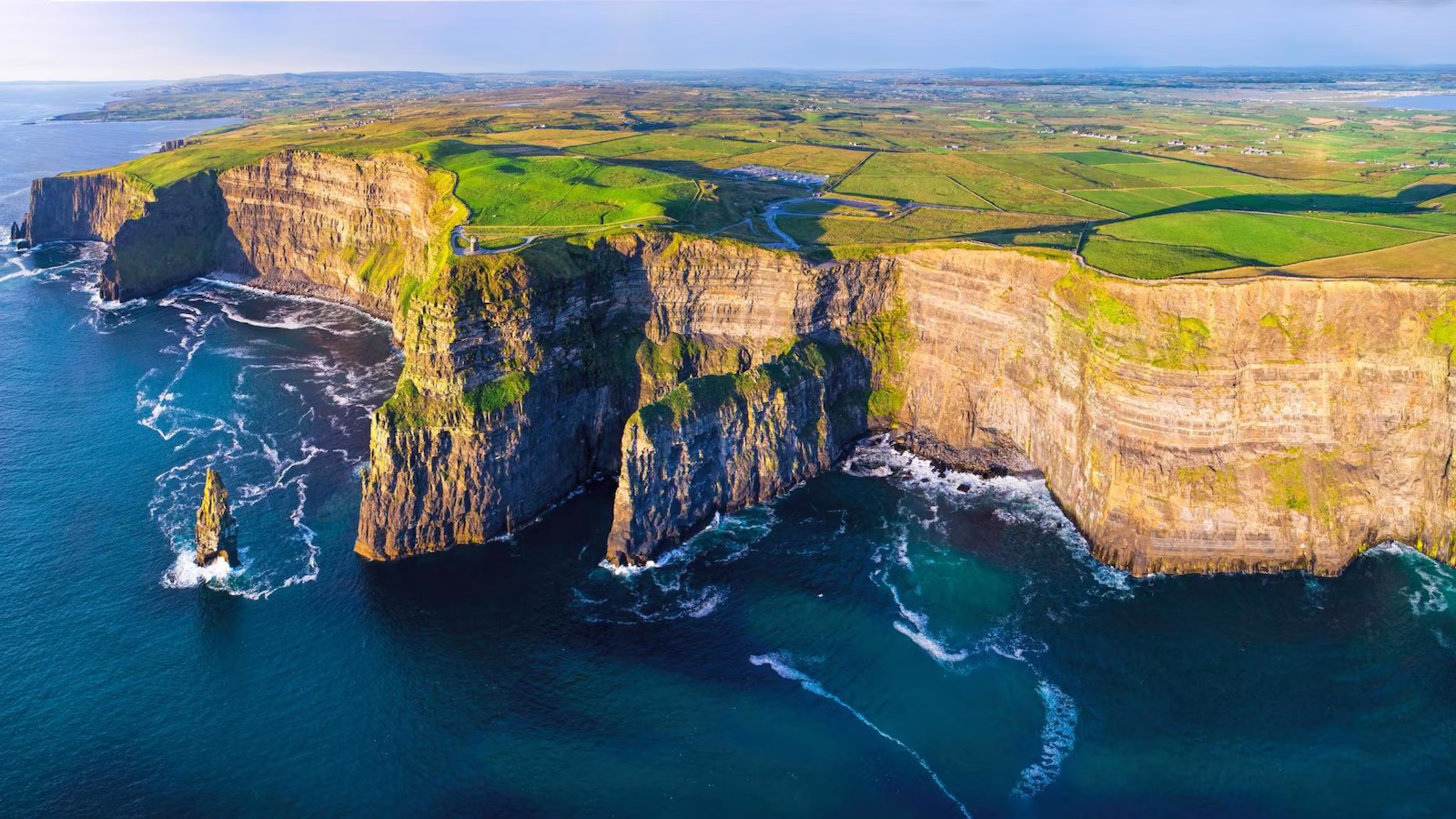 Cliffs of Moher with sea and waves crashing against cliffs and green fields in background