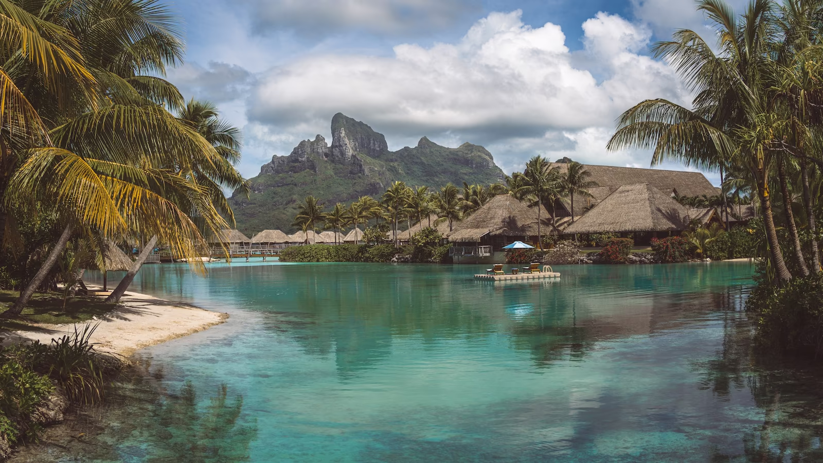 view of villas surrounded by palm trees, with blue-green water and mountains in the back