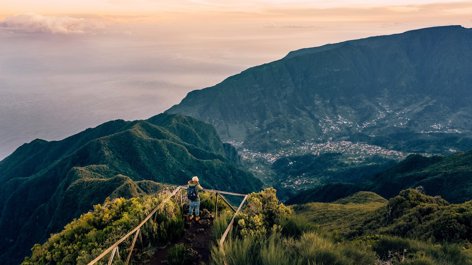person standing on the edge of a cliff overlooking villages scattered along hills near the sea