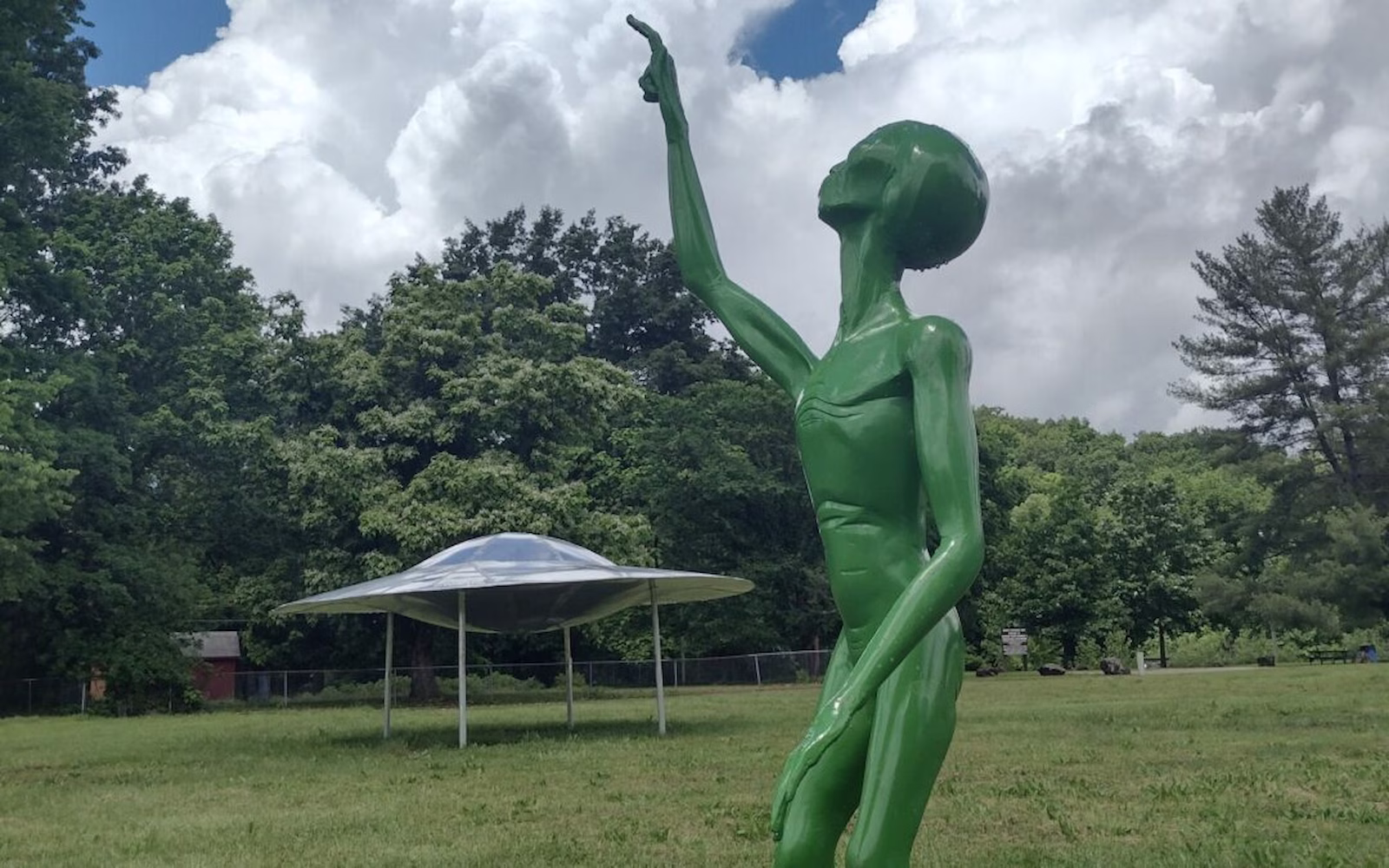 Green alien statue and UFO in park with trees