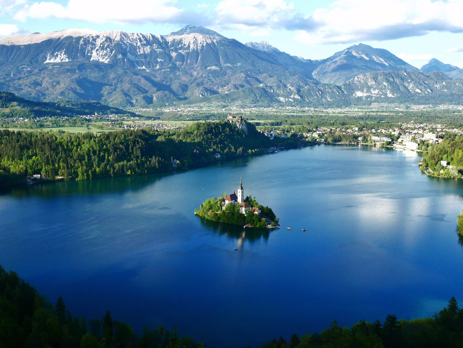 house with tower in a small island in the middle of a lake with mountain range in the background