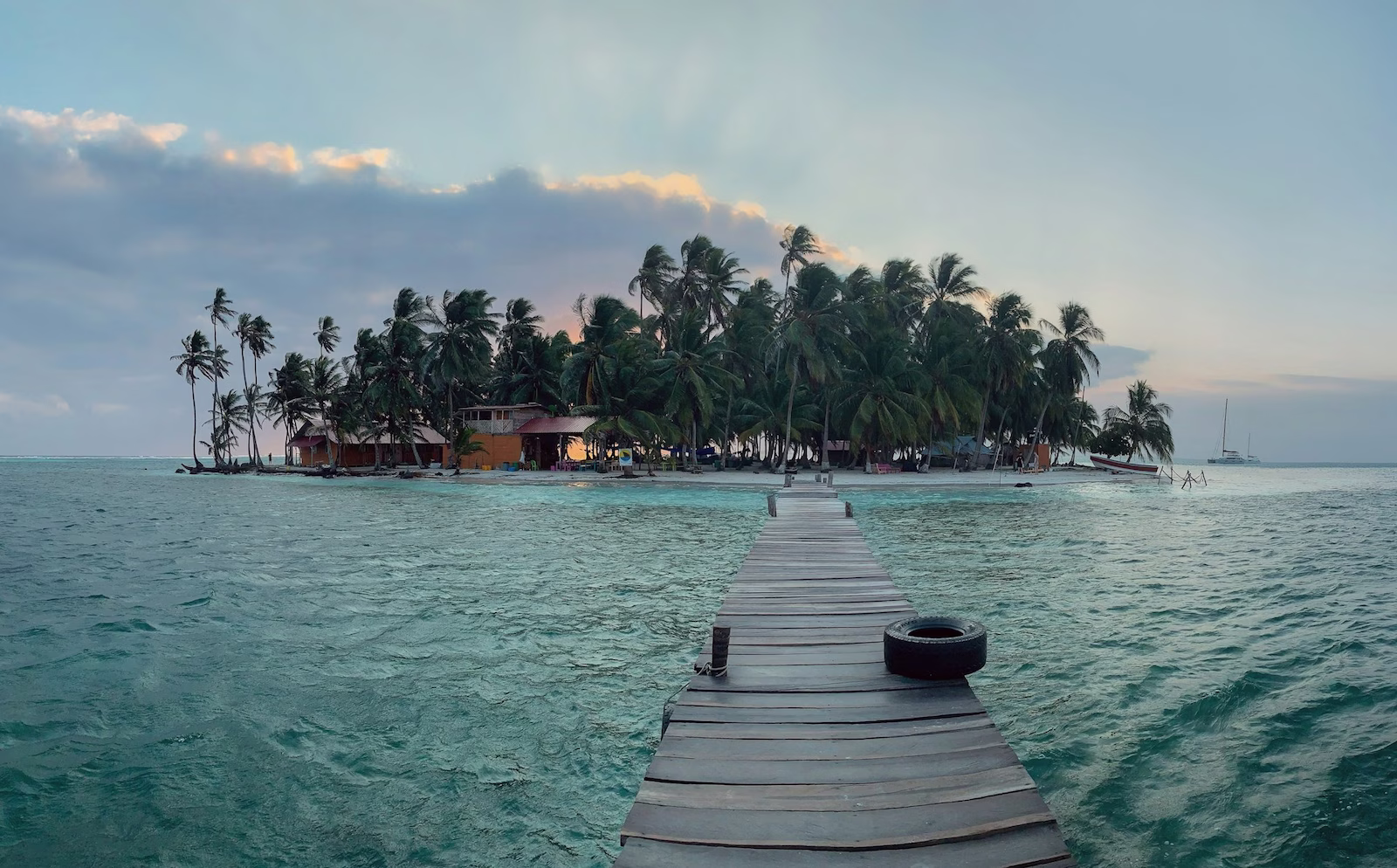 wooden bridge leading up to a small island with palm trees