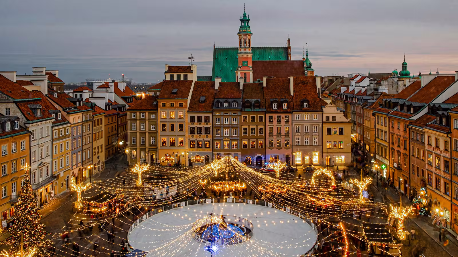 Aerial view of Christmas lights draped across town square with buildings at sunset