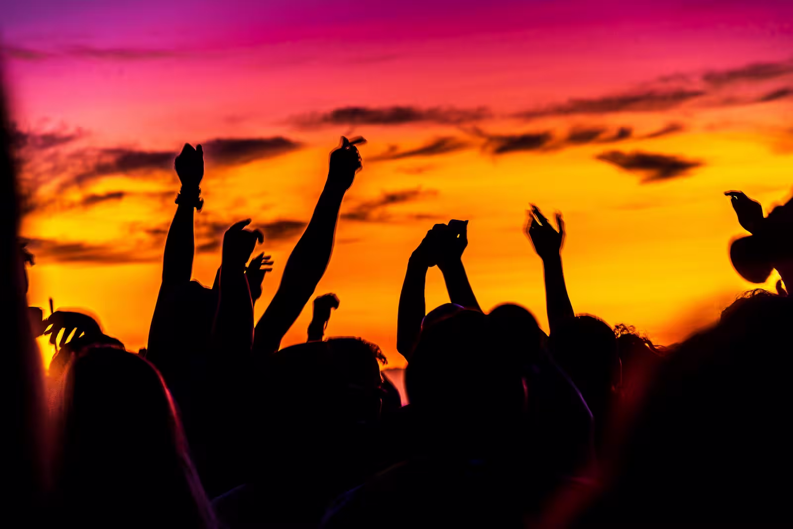silhouette of group of people with arms up in the air at sunset