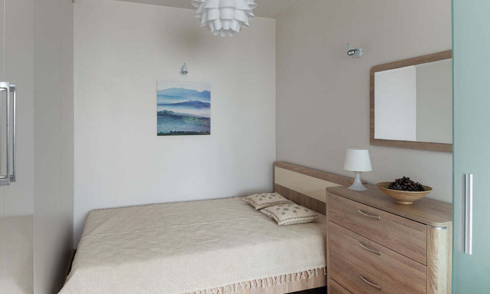 A small bedroom featuring a bed, dresser, and mirror, showcasing a cozy and functional living space.
