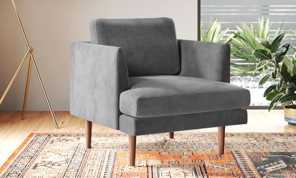 Grey velvet armchair with wooden legs placed in a cozy nook