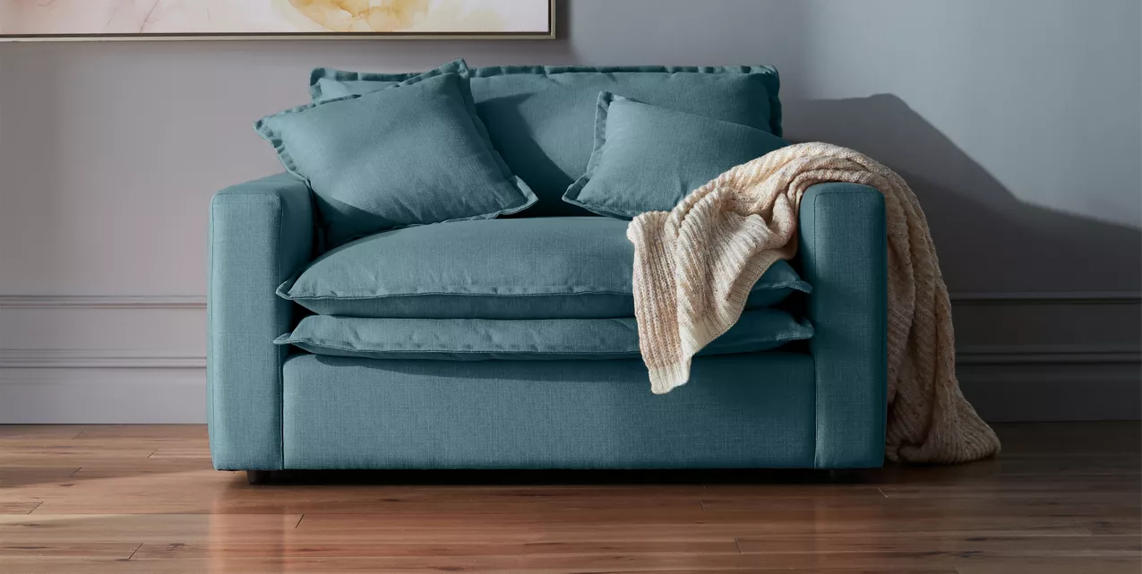 Blue oversized chair with two cushions and a white throw blanked placed near a wall