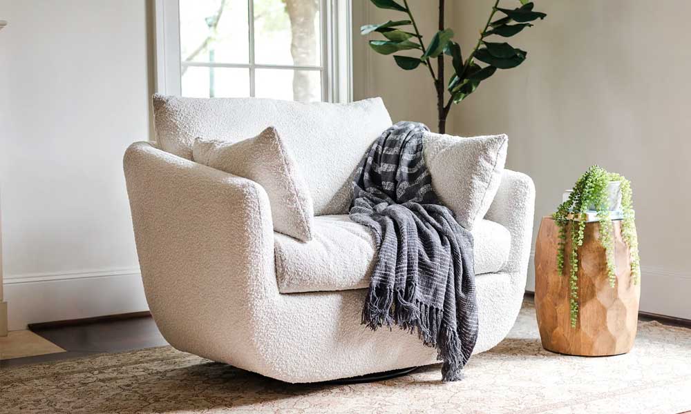 White upholstered swivel armchair with two cushions and a grey throw blanket
