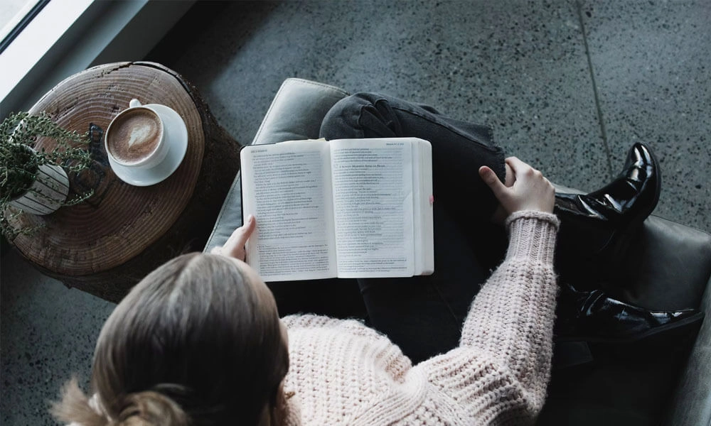 Woman reading a book sitting in a chair near a coffee table