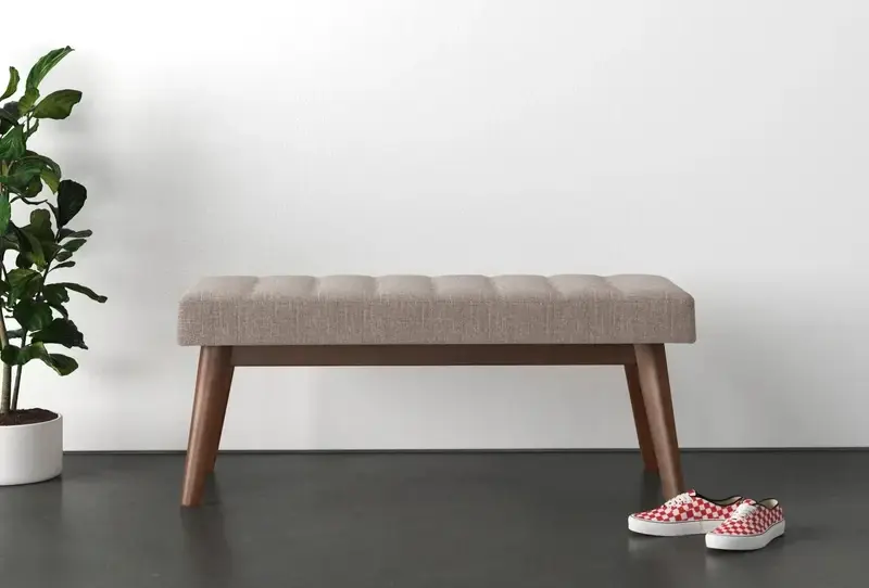 wooden bench with a grey upholstered seat cushion near a plant and shoes