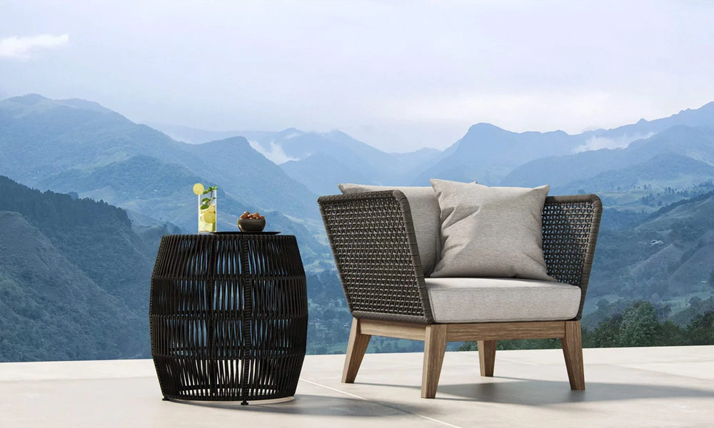A wicker lounge chair and table set against a backdrop of majestic mountains.