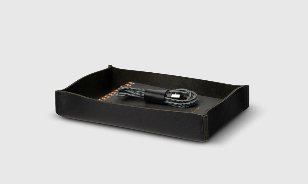 Black leather tray with a notebook and a charging cord