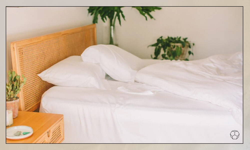 White sheetss in a bed with a wooden and rattan headboard in a bright bedroom