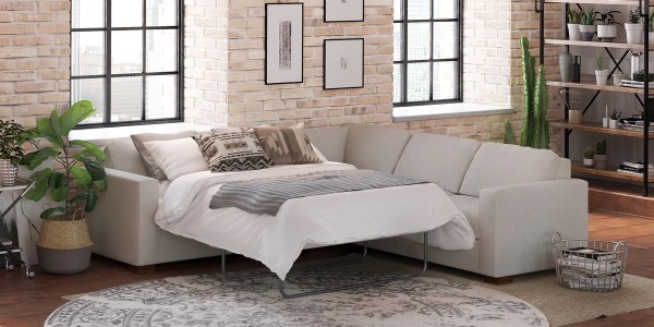 beige upholstered sleeper sectional arranged with a white duvet and pillows in a living room