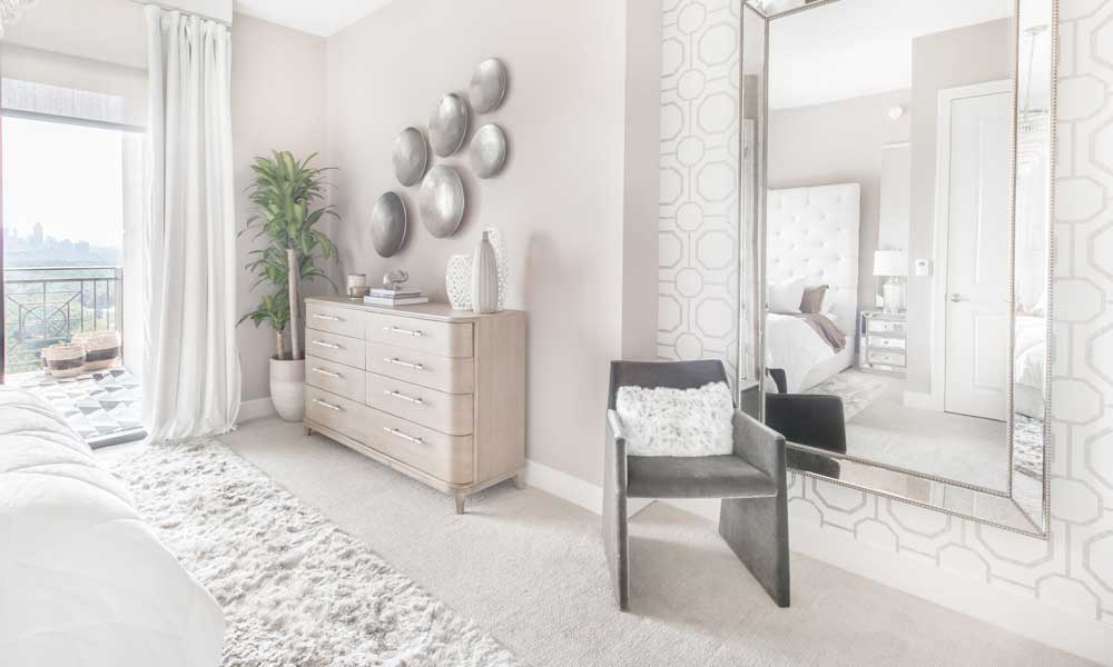 Grey acccent Chair in bedroom with white rug, bed, furniture and decor.