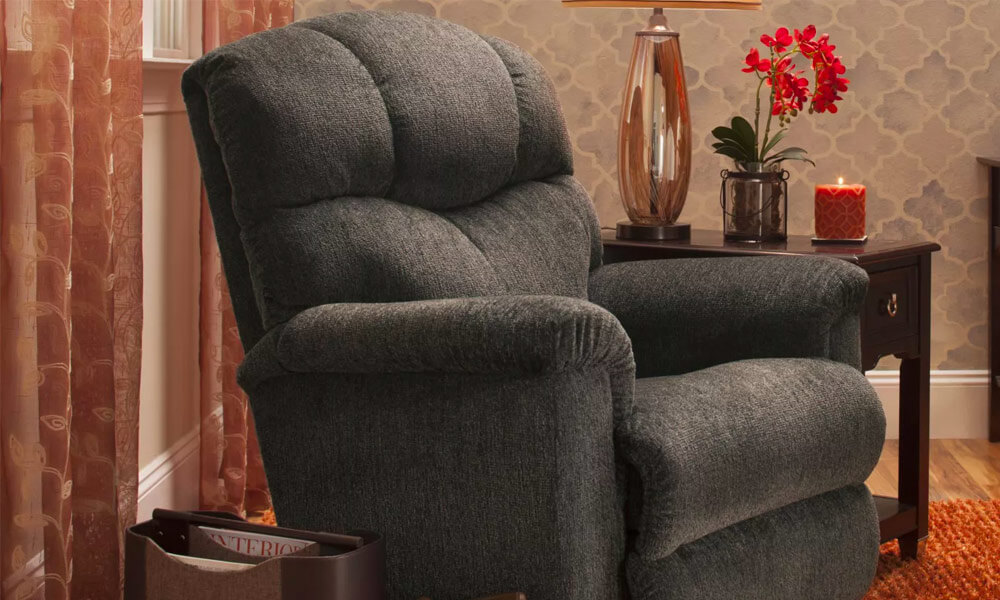 Grey upholstered Rocker Recliner near the window and orange curtains