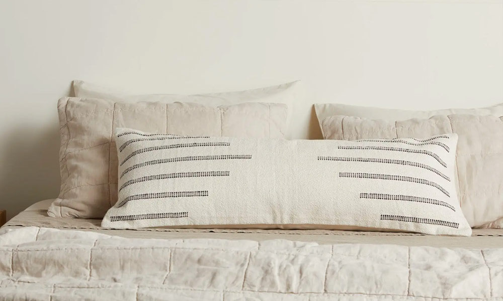 A bed with white pillows and a gray striped lumbar pillow