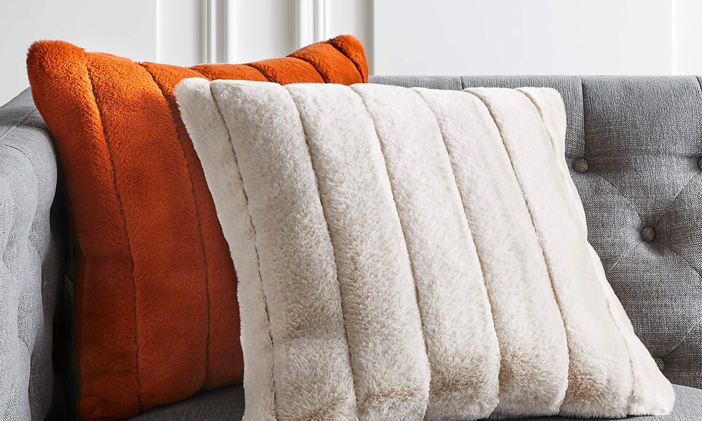 Faux fur Pillow in a grey couch, one is orange and the other one is white.