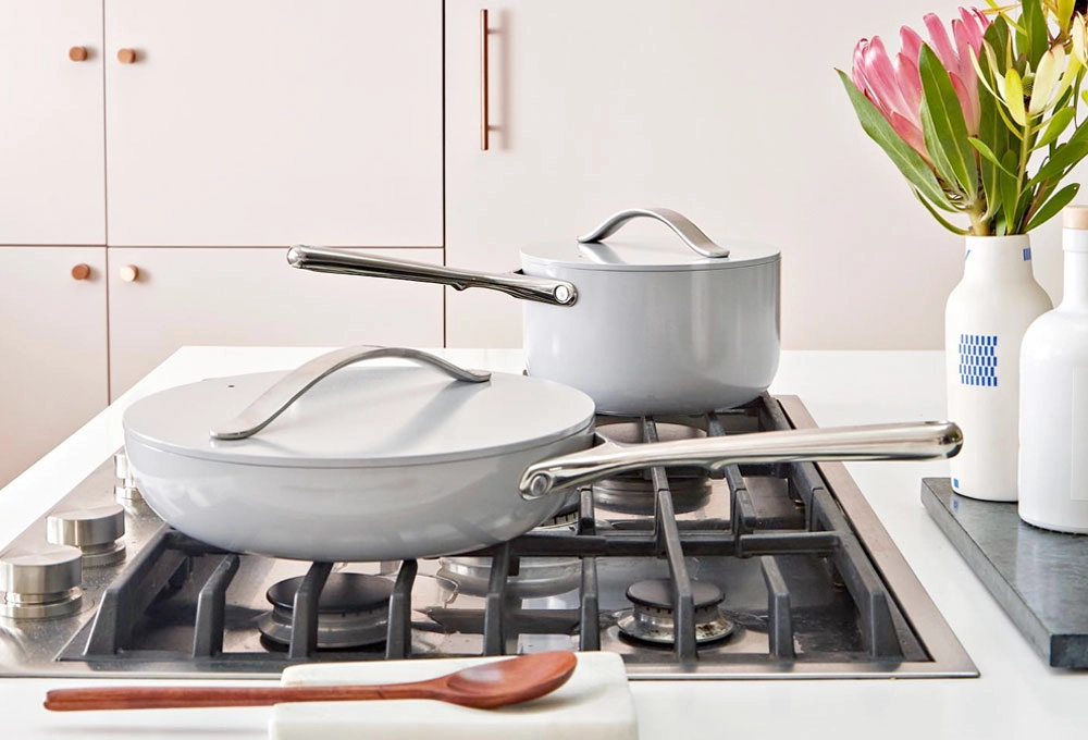 two gray saucepans with lids and stainless steel handles on a gas stove with a flower vase 